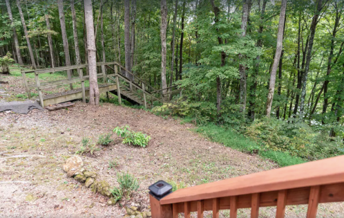 A wooden deck overlooks a wooded area with trees and a winding path leading down into the forest.