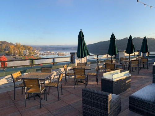 A scenic outdoor seating area with tables and umbrellas overlooking a marina and autumn foliage.