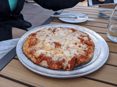 A freshly baked pizza with melted cheese and tomato sauce on a metal plate, placed on a wooden table.