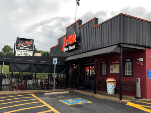 Exterior of a retro-style diner with a sign, outdoor seating, and a large ice cream cone decoration.