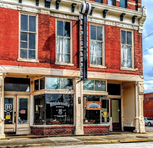 Historic brick building with large windows, featuring "Hildebrand's" sign and a welcoming storefront.