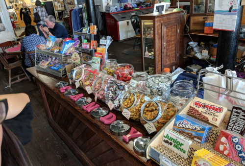 A wooden counter filled with jars of candy and snacks, with people seated in the background.