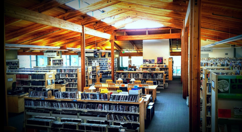 A spacious library interior with wooden beams, shelves of books, and study areas filled with chairs and tables.