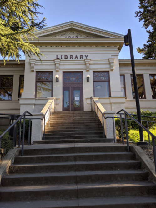 Front entrance of a library with steps leading up to large double doors and decorative architecture.