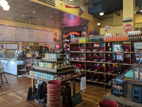 A colorful ice cream shop interior with a menu board, shelves of treats, and a display of candles and merchandise.