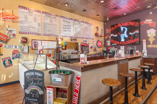 A vintage soda fountain shop with colorful signs, a menu board, and a display of ice cream and drinks.