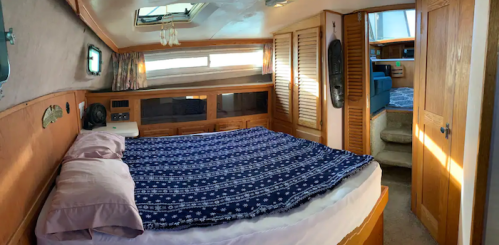 Cozy interior of a boat cabin featuring a large bed, wooden paneling, and natural light from a window.