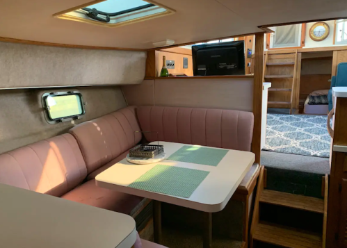 Interior of a cozy boat cabin featuring a pink seating area, a table, and a staircase leading to another room.