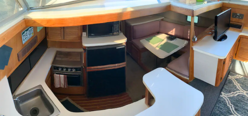 Interior of a boat featuring a kitchen area with a sink, microwave, stove, and a cozy dining space.