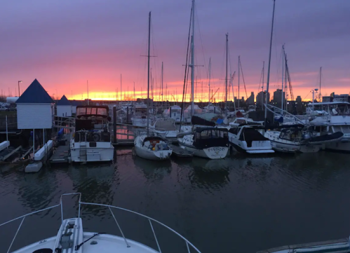Sunset over a marina with sailboats and yachts silhouetted against a colorful sky.