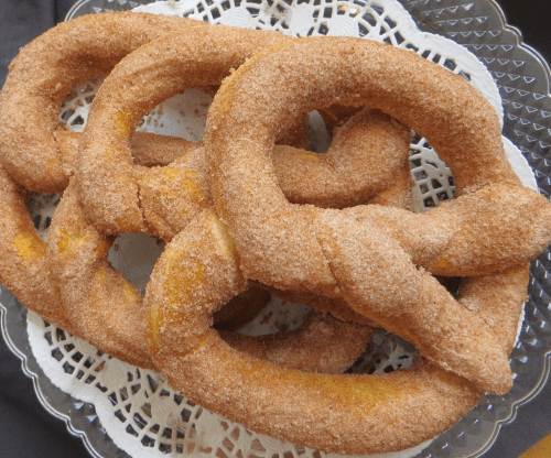 A plate of cinnamon-sugar coated pretzels arranged on a lace doily.