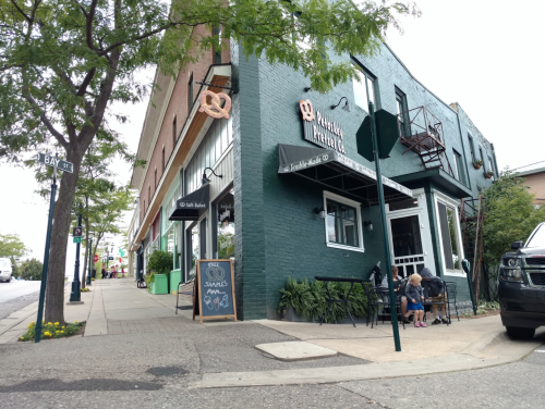 A corner building with a café, outdoor seating, and a chalkboard sign, surrounded by trees and a sidewalk.