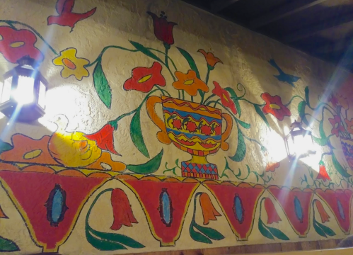 Colorful mural featuring a floral design with a vase, flowers, and decorative patterns on a textured wall.