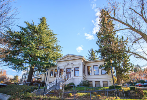 A historic library building surrounded by tall trees under a clear blue sky.