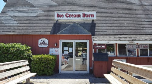 Exterior of the Ice Cream Barn, featuring a red wooden facade, large glass doors, and outdoor seating.