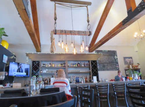 A cozy bar interior with wooden beams, a well-stocked bar, and patrons enjoying the space. Warm lighting adds ambiance.