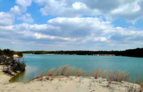 A serene lake surrounded by sandy shores and lush greenery under a partly cloudy sky.