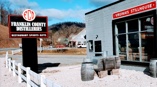 Sign for Franklin County Distilleries with a building and barrels outside, set against a clear blue sky.