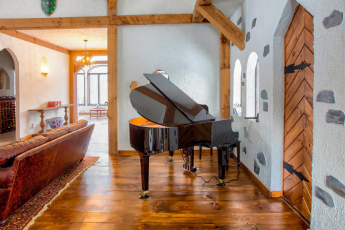 A grand piano in a cozy room with wooden beams, a sofa, and stone accents, creating an inviting atmosphere.
