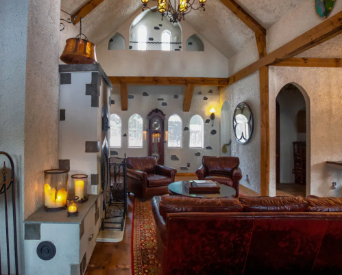 Cozy living room with leather sofas, a round table, candles, and rustic decor featuring wooden beams and arched windows.