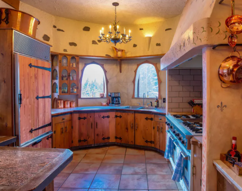 Cozy kitchen with wooden cabinets, a curved layout, and large windows, featuring a stove and decorative lighting.