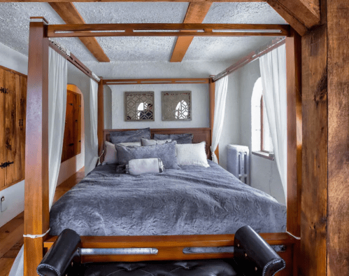 Cozy bedroom featuring a wooden four-poster bed with gray bedding and decorative wall accents.