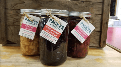 Three jars of pie filling labeled apple, marionberry, and tart cherry, displayed on a wooden surface.