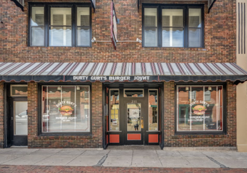 Exterior of Durty Gurt's Burger Joynt, featuring a brick facade and striped awning, with large windows displaying the restaurant's name.
