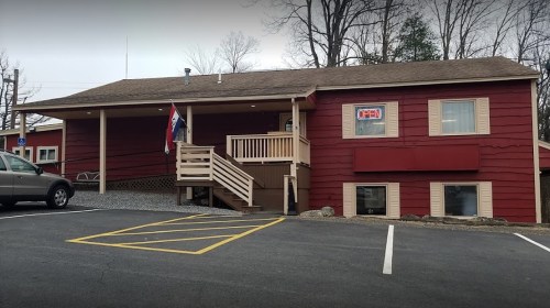 A red wooden building with a sign that says "OPEN," featuring a staircase and parked car in front.