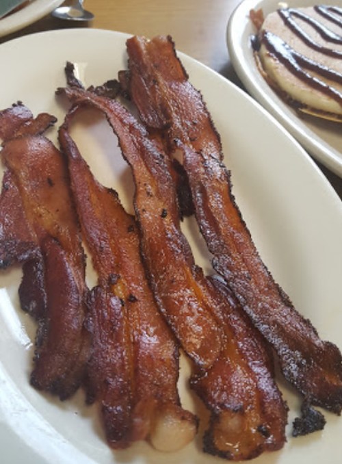 A plate of crispy, cooked bacon strips arranged neatly.