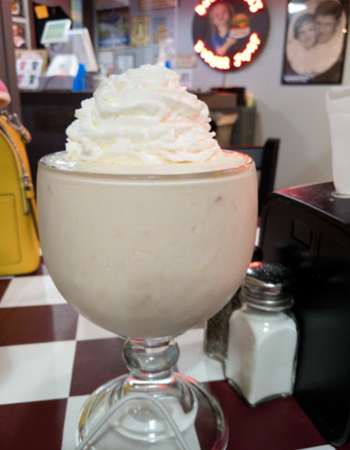 A large glass filled with creamy vanilla ice cream topped with whipped cream, set on a checkered table.