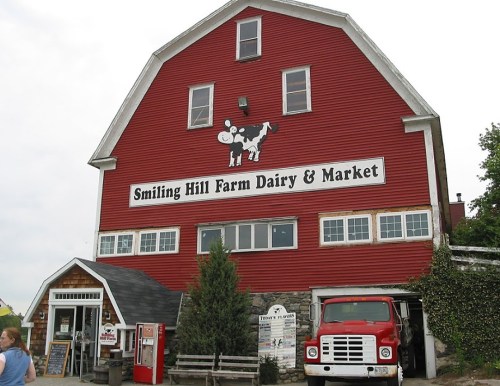 Red barn with "Smiling Hill Farm Dairy & Market" sign, featuring a cow logo and a red truck parked outside.