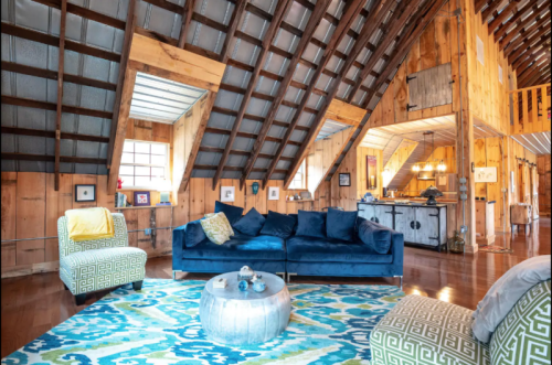 Cozy living room with a blue sofa, patterned rug, wooden walls, and a lofted ceiling, featuring warm, rustic decor.