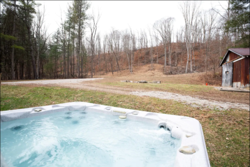 A hot tub in the foreground with a wooded area and a rustic shed in the background on a cloudy day.