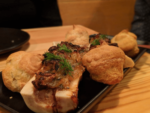 A plate of roasted bone marrow topped with herbs, accompanied by small pastries on a wooden table.