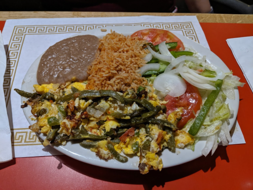 A plate of scrambled eggs with green beans, served with rice, refried beans, and a fresh salad of tomatoes and onions.