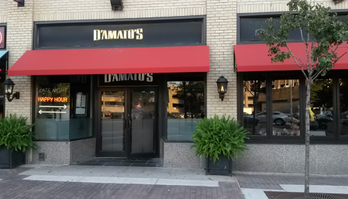 Exterior of D'Amato's restaurant featuring red awnings, large windows, and a sign for late night happy hour.