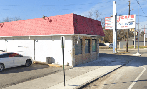 A small soul food restaurant with a red roof and signage, located on a street corner with a parked car nearby.