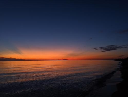 A serene sunset over calm waters, with vibrant orange and purple hues reflecting on the surface.
