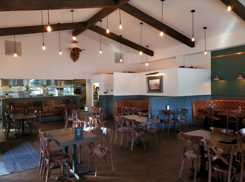 Cozy restaurant interior with wooden beams, dim lighting, and leather seating, featuring a rustic decor style.