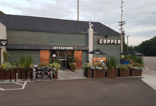 Exterior of a restaurant named "Copper," featuring outdoor seating, planters, and bicycles parked nearby.