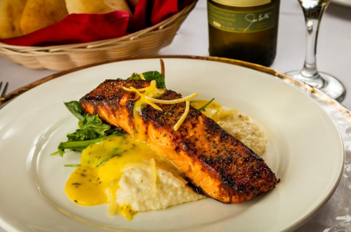 A beautifully plated salmon fillet on a bed of creamy grits, garnished with lemon and served with greens.