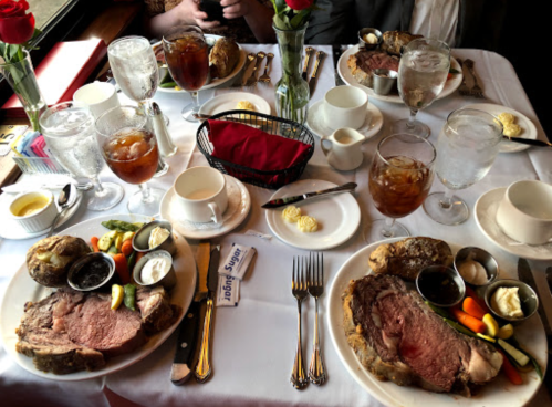 A table set with four plates of prime rib, sides, drinks, and flowers, creating an inviting dining atmosphere.