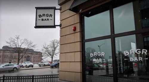Exterior view of BRGR Bar with large windows, snowy weather, and parked cars in the background.