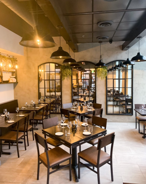 A cozy restaurant interior with wooden tables, chairs, and large mirrors, featuring warm lighting and a welcoming atmosphere.