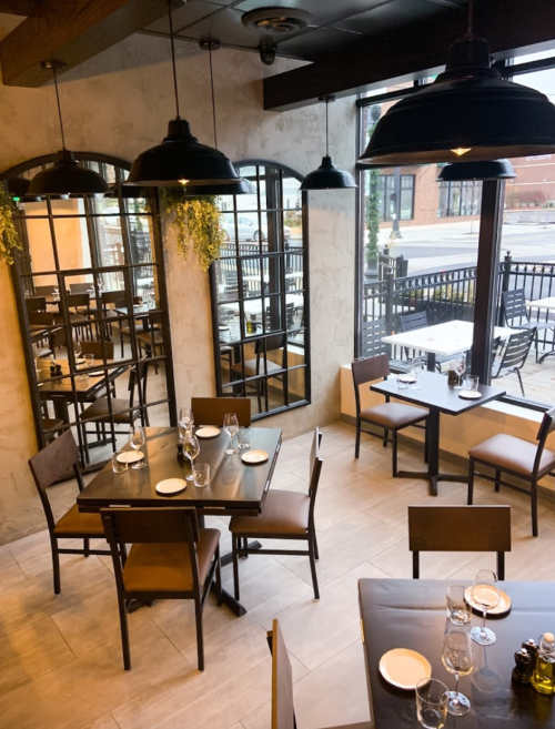 A cozy restaurant interior with wooden tables, chairs, and large mirrors, featuring a view of the outdoor patio.