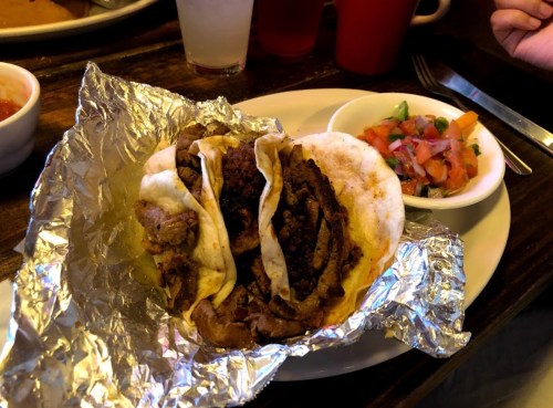 Three tacos filled with beef, served on a plate with a side of fresh salsa and pico de gallo.