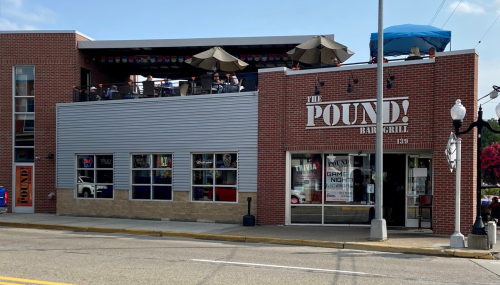 Exterior view of The Pound! Bar & Grill, featuring a rooftop patio and large windows, located on a busy street.