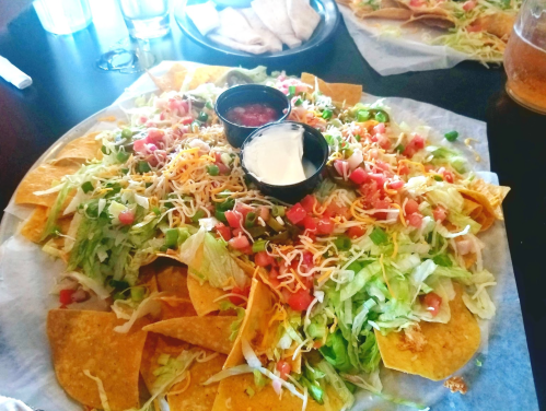 A large plate of nachos topped with lettuce, tomatoes, cheese, and served with salsa and sour cream in small bowls.