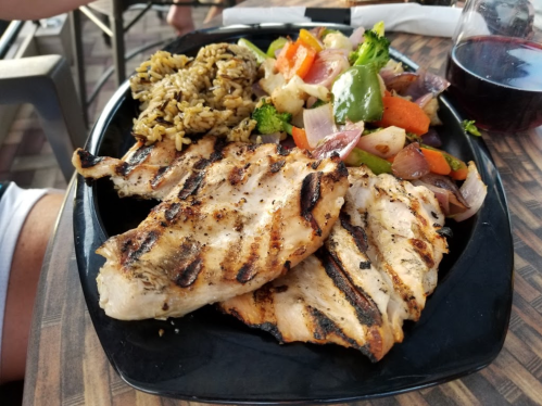 Grilled chicken breast served with rice and a colorful vegetable medley on a black plate.